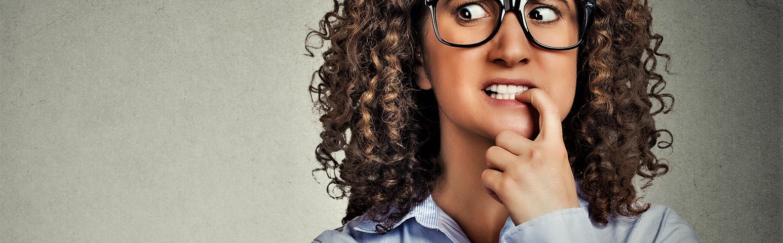 anxious girl with brown curly hair wearing glasses and blue shirt with finger in her mouth