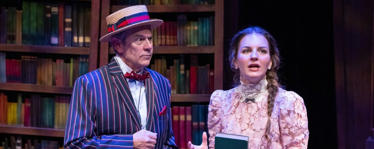 A man in a blue pinstripe jacket and a straw boater hat looks at a woman with brown hair in a braid and a lacy pink shirt who is speaking and holding a green book.