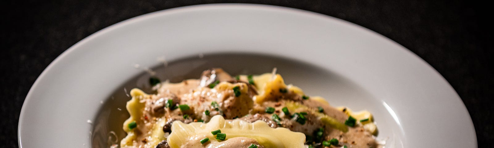 An image of Ravioli in mushroom cream sauce in a shallo pasta bowl