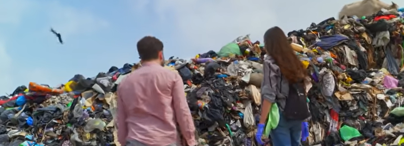 two people stand before a mountain of clothes