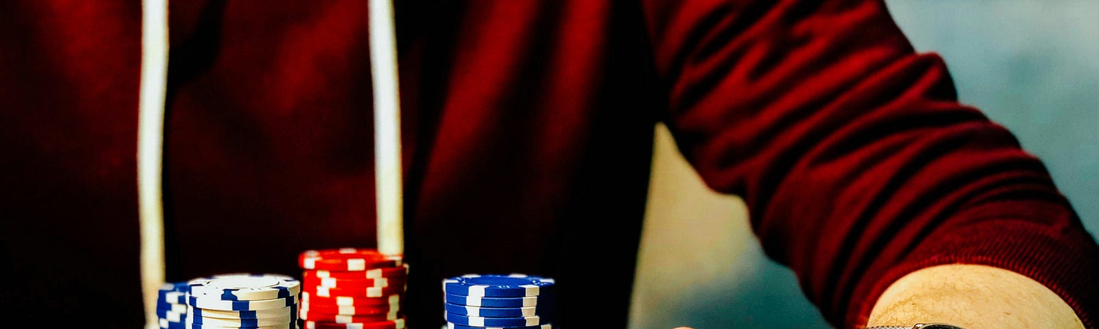 A man wearing a red sweater, playing poker, his chips stacked in front of him; his hand is on two unplayed cards, with chips on them.