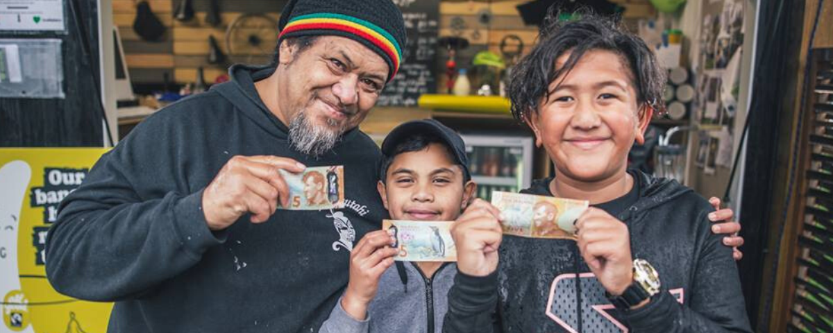 A man and two tama (boys) holding five dollar bills and smiling to camera
