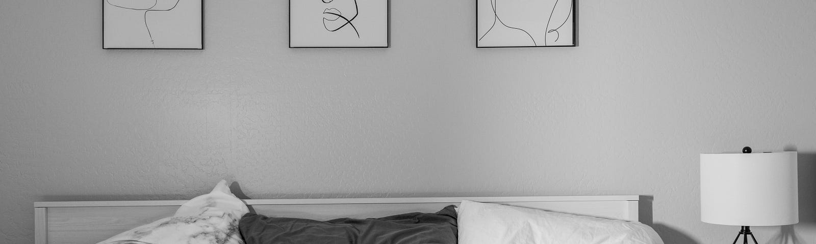 Rumpled cotton sheets on a queen sized bed with three different pillows at the head. Monochrome palette, gray and white.