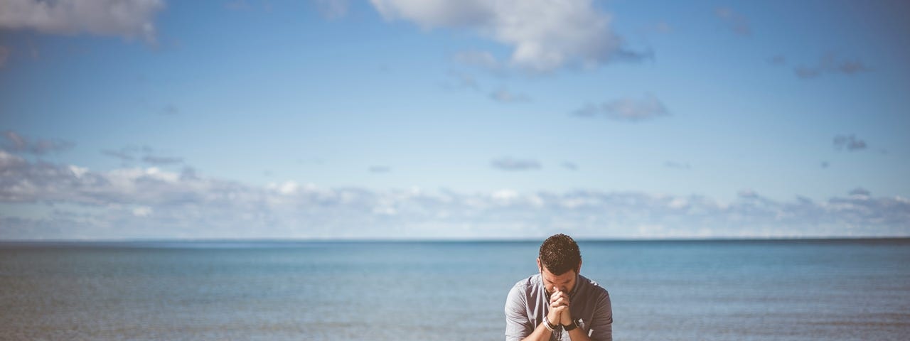 A man kneeling on the beach in prayer