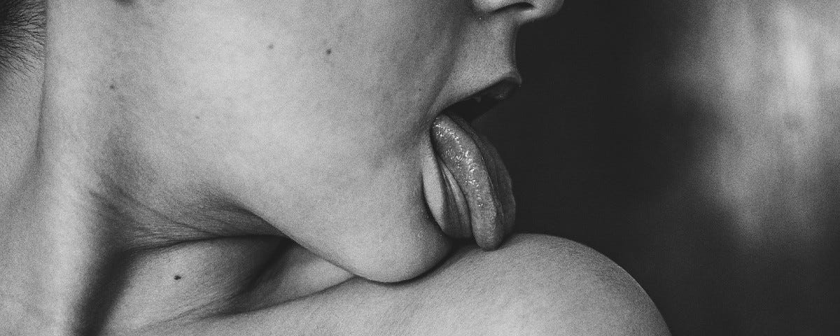 A monochrome closeup of a woman with her head turned to lick her naked shoulder.