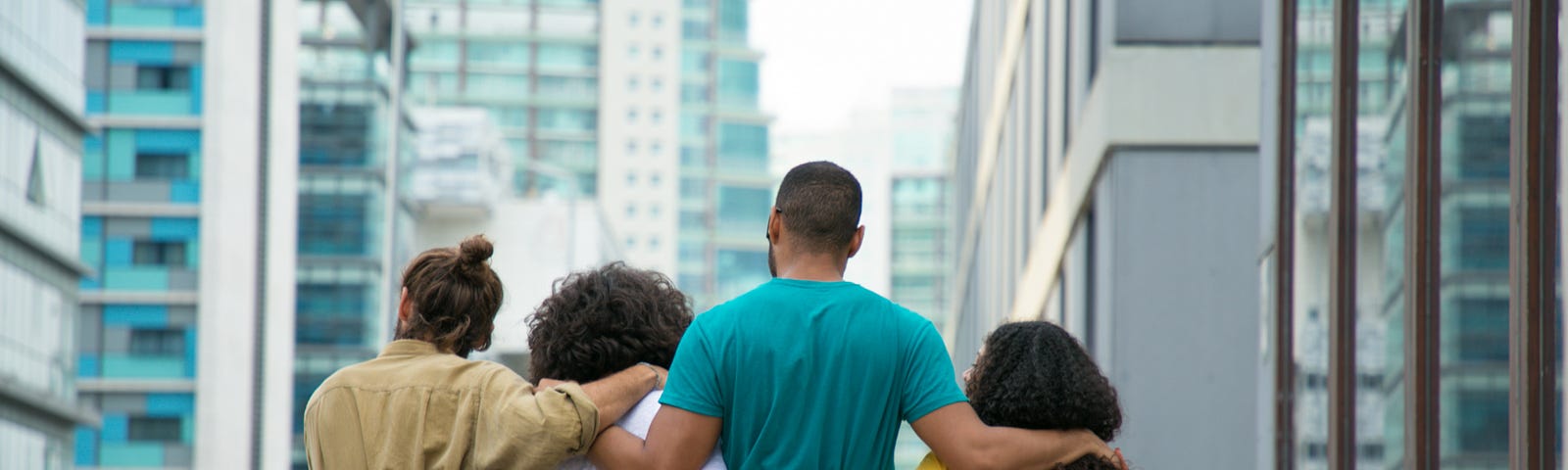 A group of four people, two men and two women, stand with their arms around each other with their backs to the camera. They are looking out across a city.