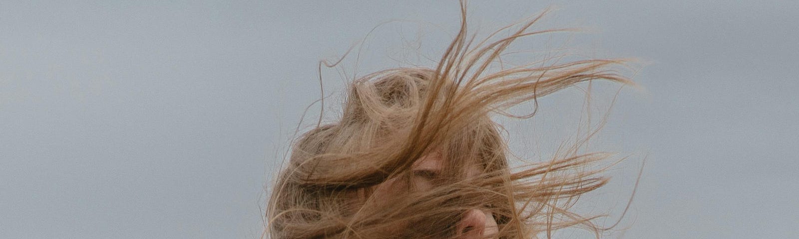 A woman with windy hair standing on a seashore with cloudy sky