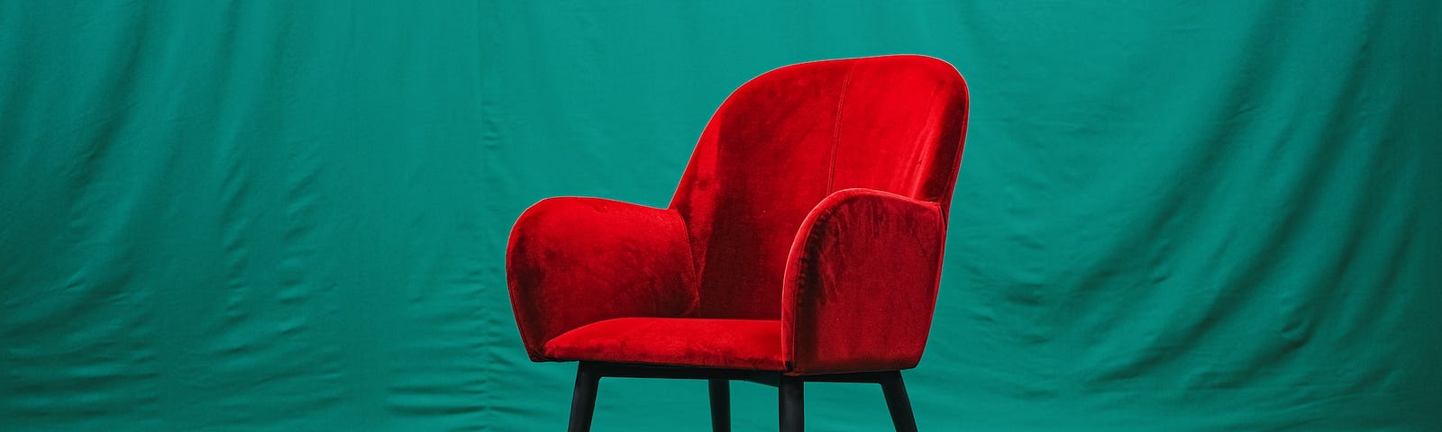 A red velvet chair with arms on a dark green floor and backdrop