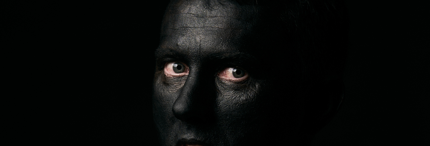 Halloween makeup portrait of a young man with black face and slit throat