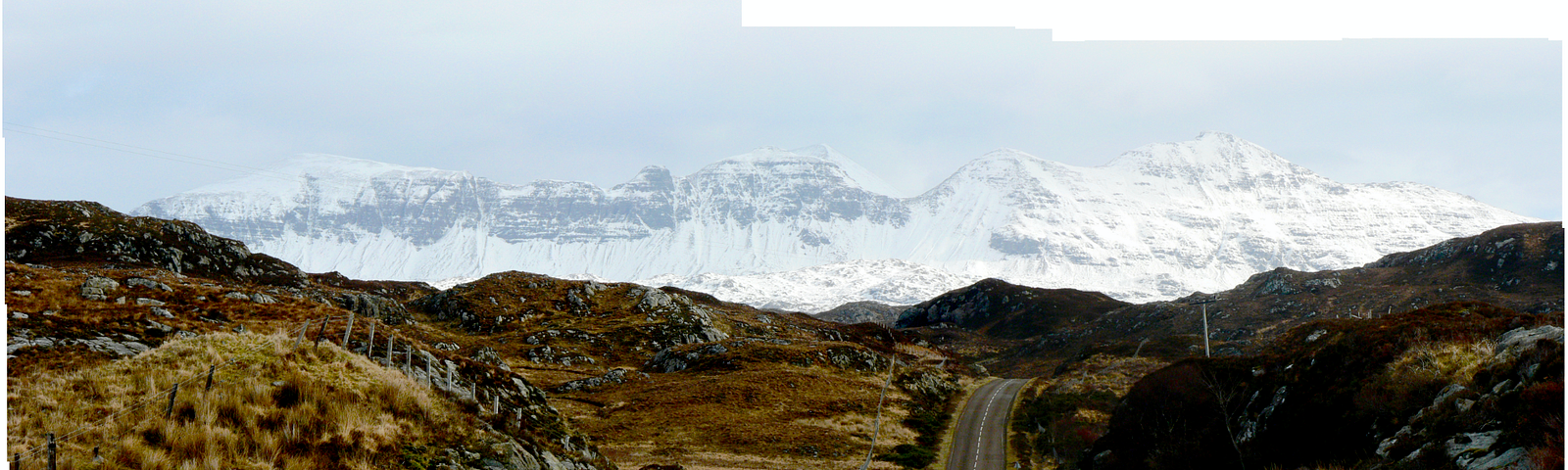 A panorama of a road receding into a background of snowy mountains
