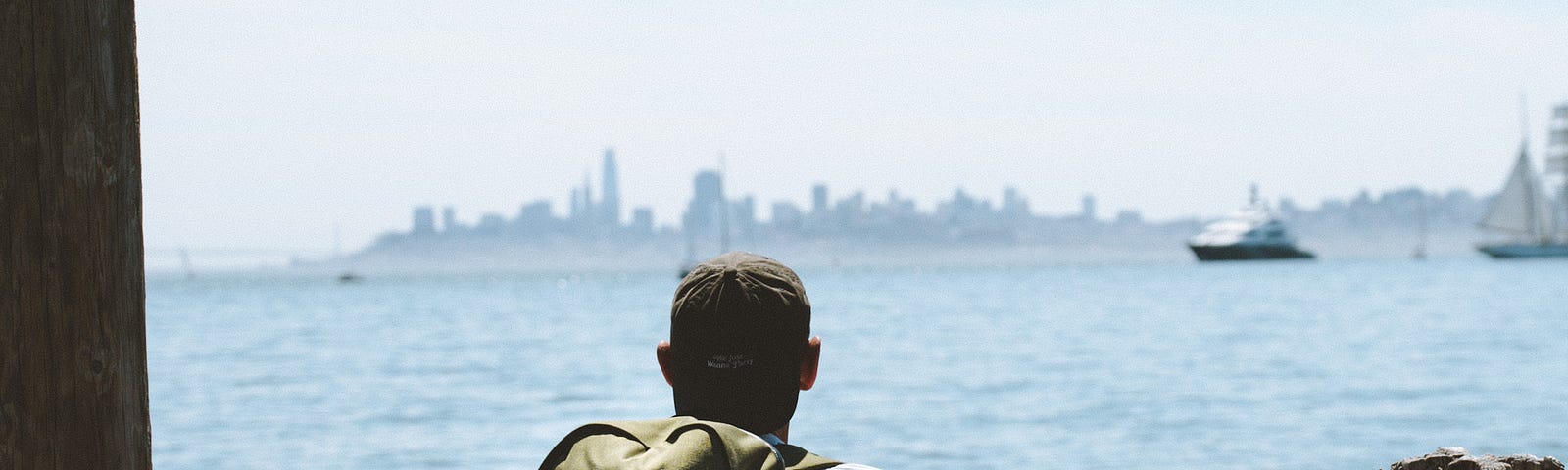 A man sitting on a bench wearing the MTW Backpack looking at San Francisco.