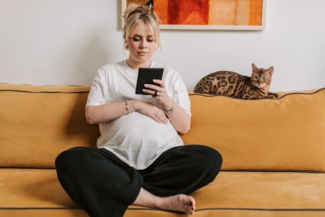 A pregnant woman sitting on a sofa with her cat