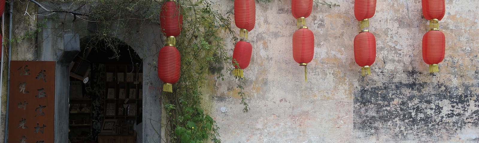 Typical Chinese building with door opening. Red lanterns hanging down and Chinese characters written vertically next to the door.