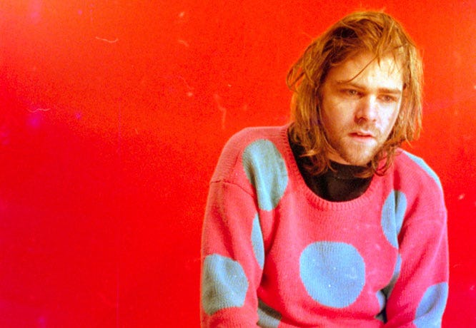 Ariel Pink looking sad in a pink sweater with blue polka dots and a blazing red background.