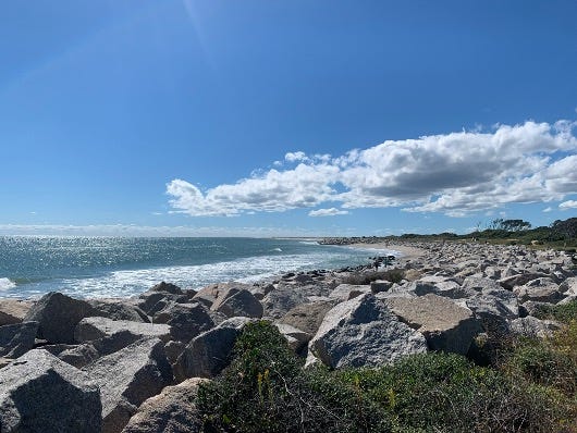 image of rocky beach, ocean water with sunlight on the waves, white clouds in the blue sky