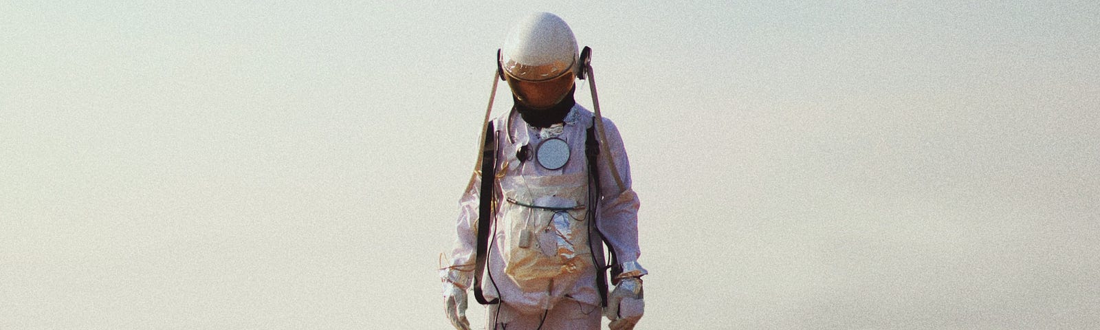 A lone astronaut looks down sadly while standing in a golden field.