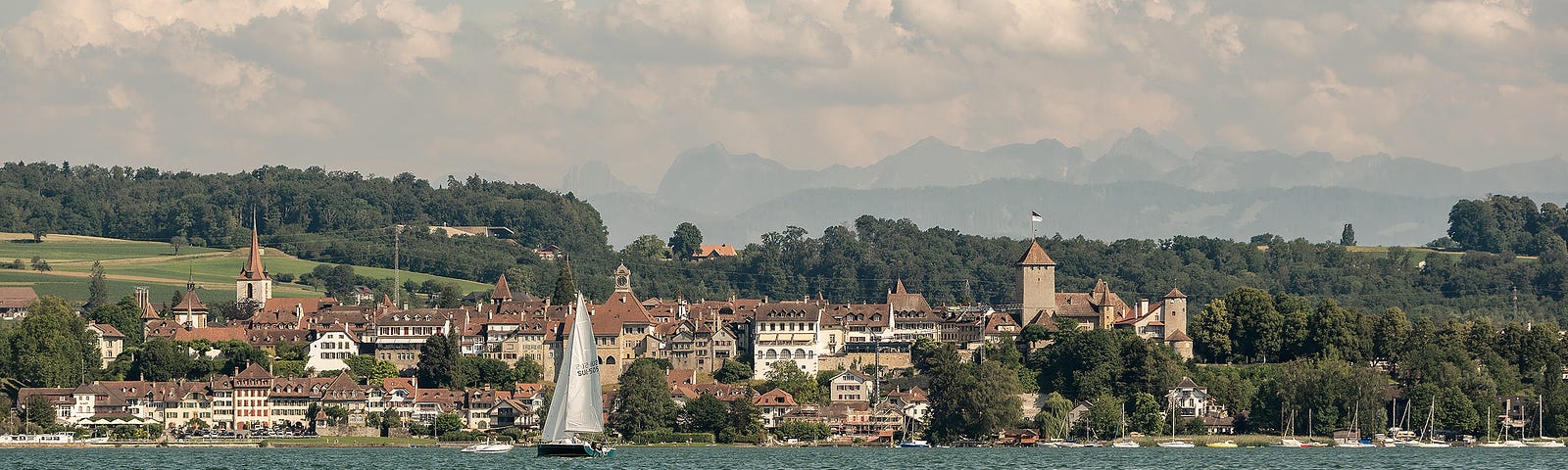 Blick vom See auf die Stadt Murten und die dahinter liegenden Hügelzüge.