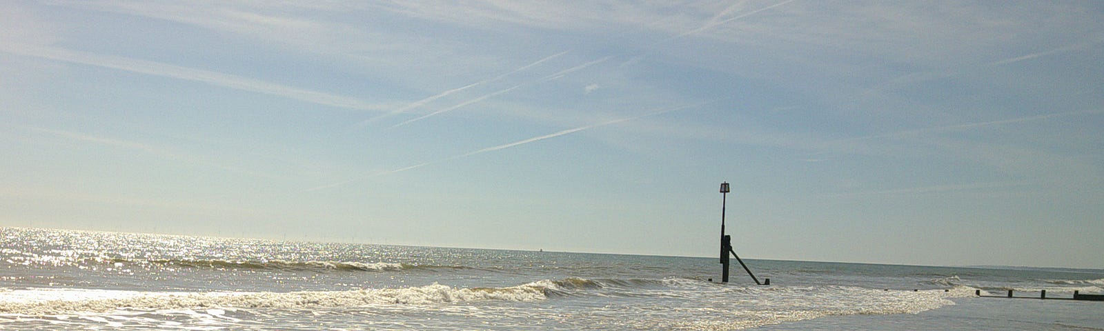 Photograph of early morning sunrise with the summer sun shining over the North Sea with the waves rippling ashore onto the beach and blue sky in the background