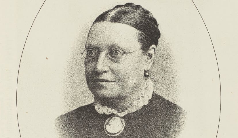 Head and shoulders photographic portrait of a Victorian woman wearing round glasses and a cameo brooch.