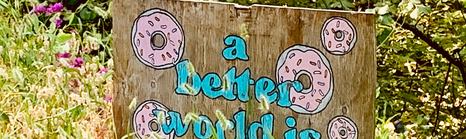 Hand painted plywood sign with donuts and the phrase, “a better world is possible”