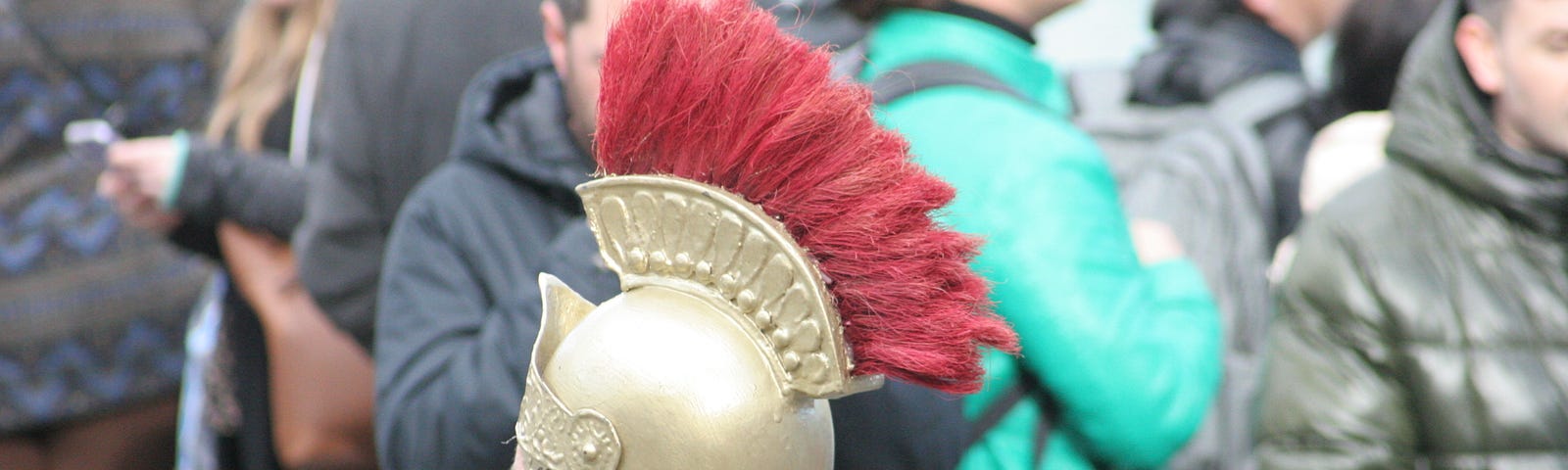 Gold centurion’s helmet with red crest against a background of people