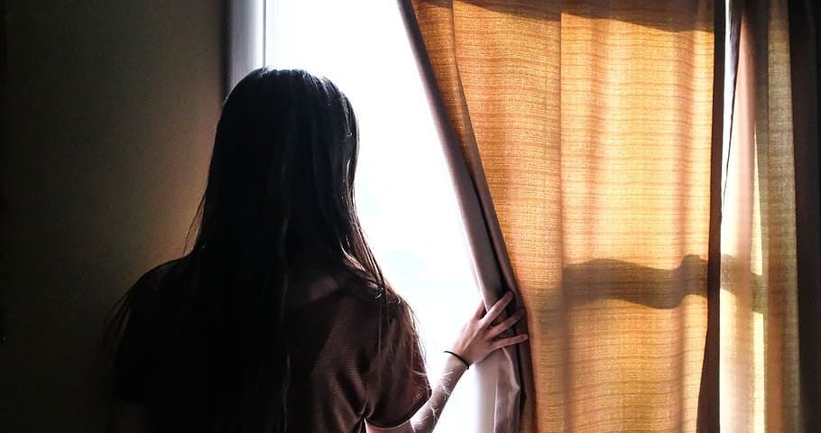 A woman looking out of a window through the curtains.