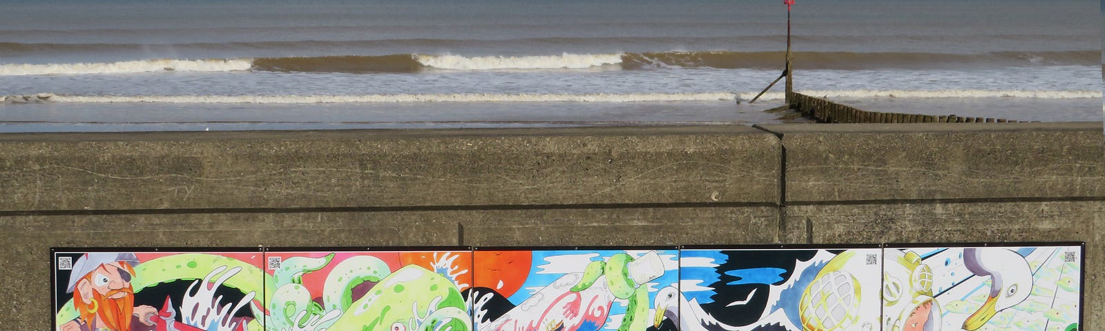 Cartoonish art on a grey retaining sea wall, with waves beyond.