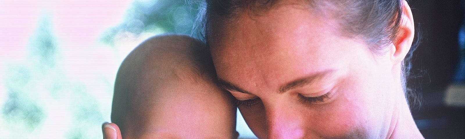 A mother cradles an infant holding her forehead against her own