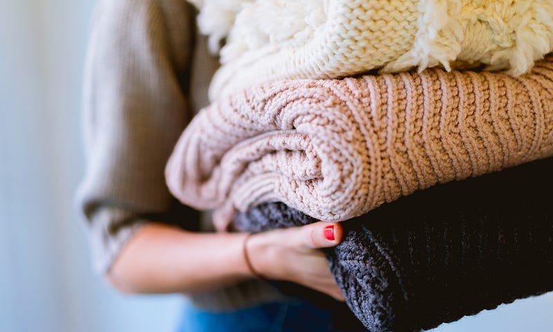 A woman holding three folded cozy sweaters