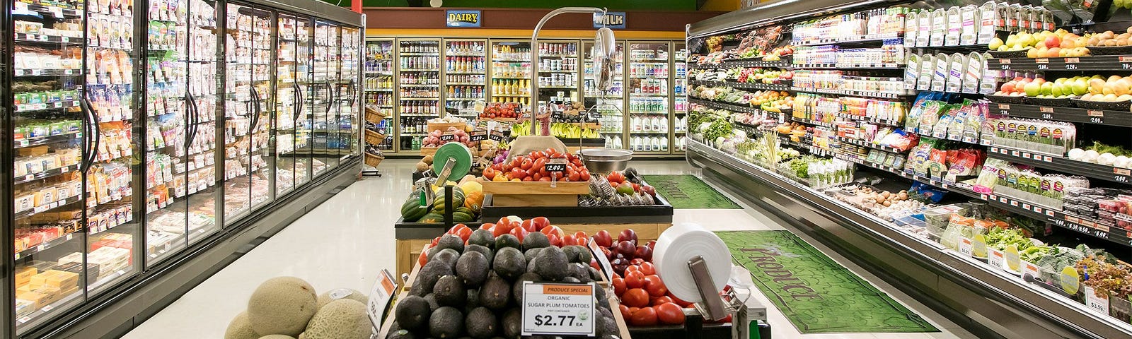 A supermarket isle with fruits, vegetables and a fridge section.