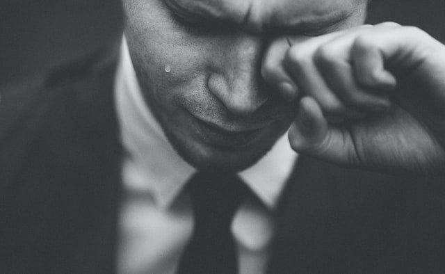 A man in a suit crying and wiping the tear from one eye.