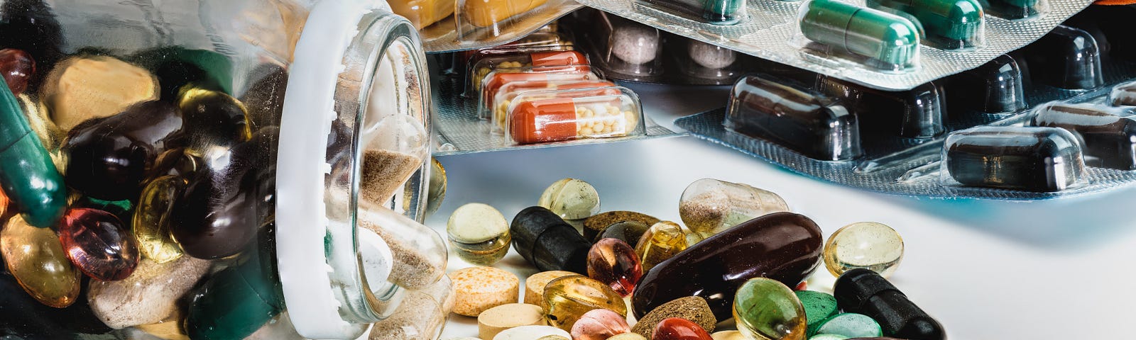 A selection of pill bubble packs and a pill bottle with pills strewn across the table.