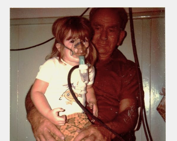 Girl sitting on her Pop’s lap having a nebuliser