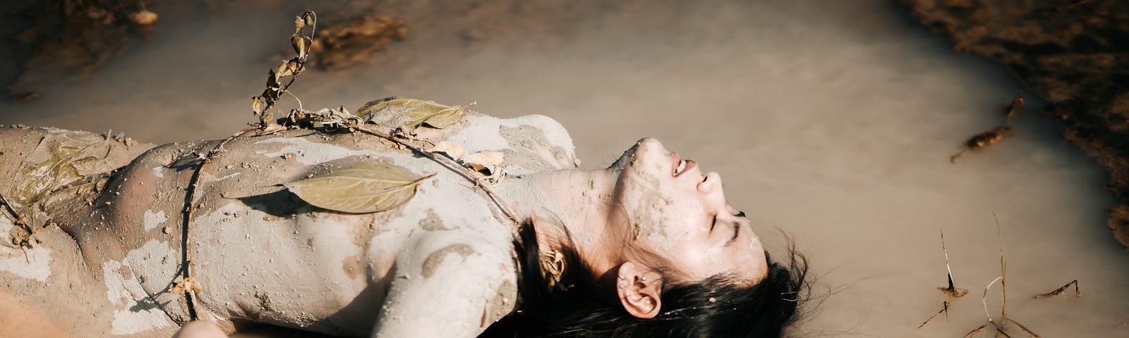 What seems to be the naked body of a woman lying in some shallow water. It is hard to tell if she is naked though, as she has mud and leaves across her torso.