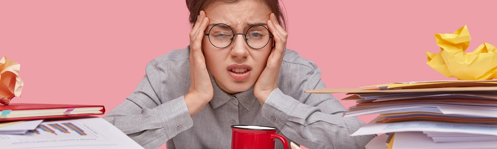 woman sitting at desk holding her head, looking overwhelmed