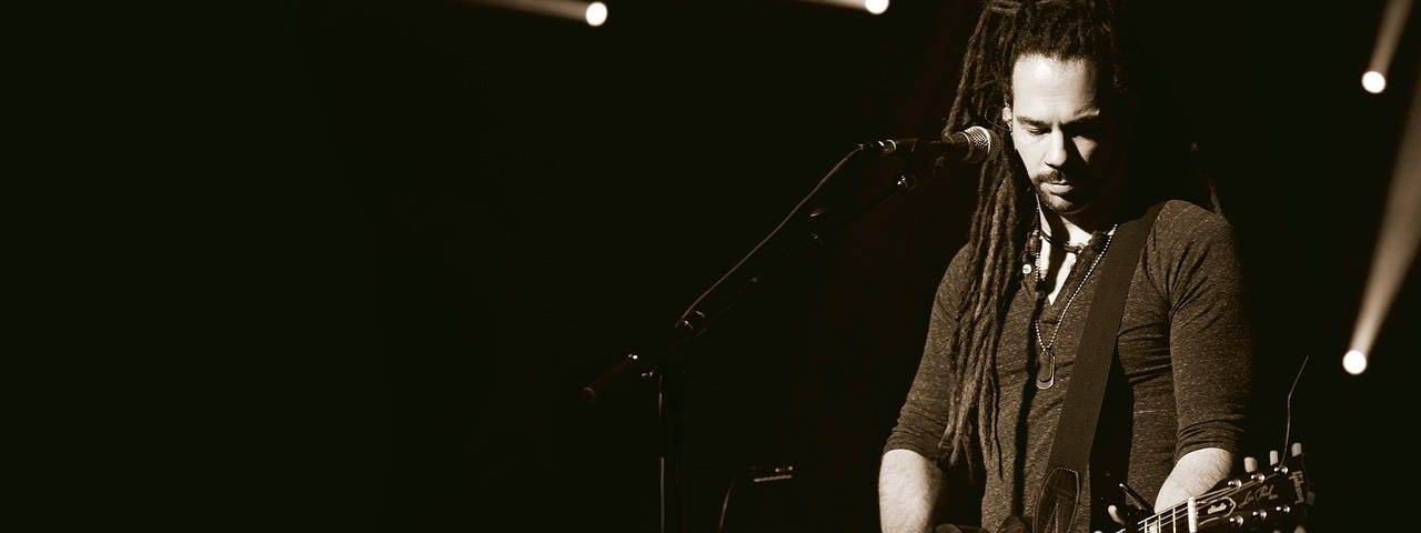 Man with goatee beard plays guitar on stage