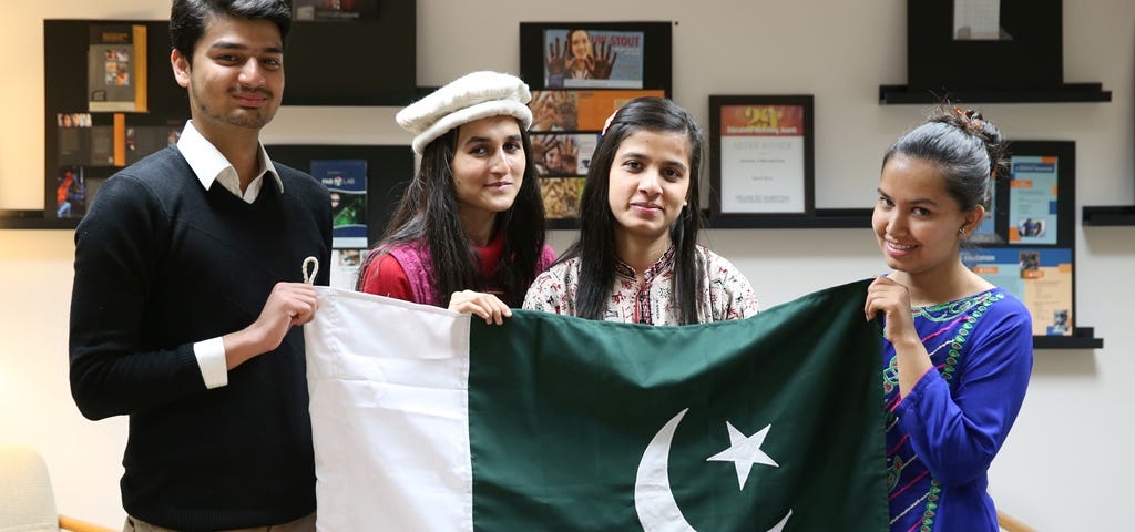 Three Girls and a boy holding a Pakistani flag with handicrafts on a table