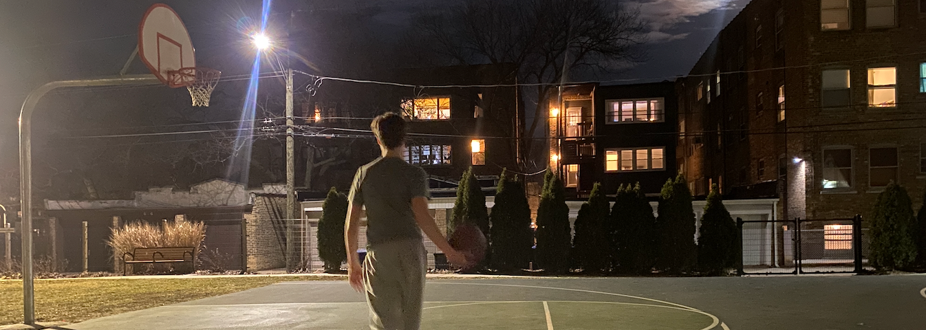 boy walking towards basketball hoop in the dark at park. The moon is glowing