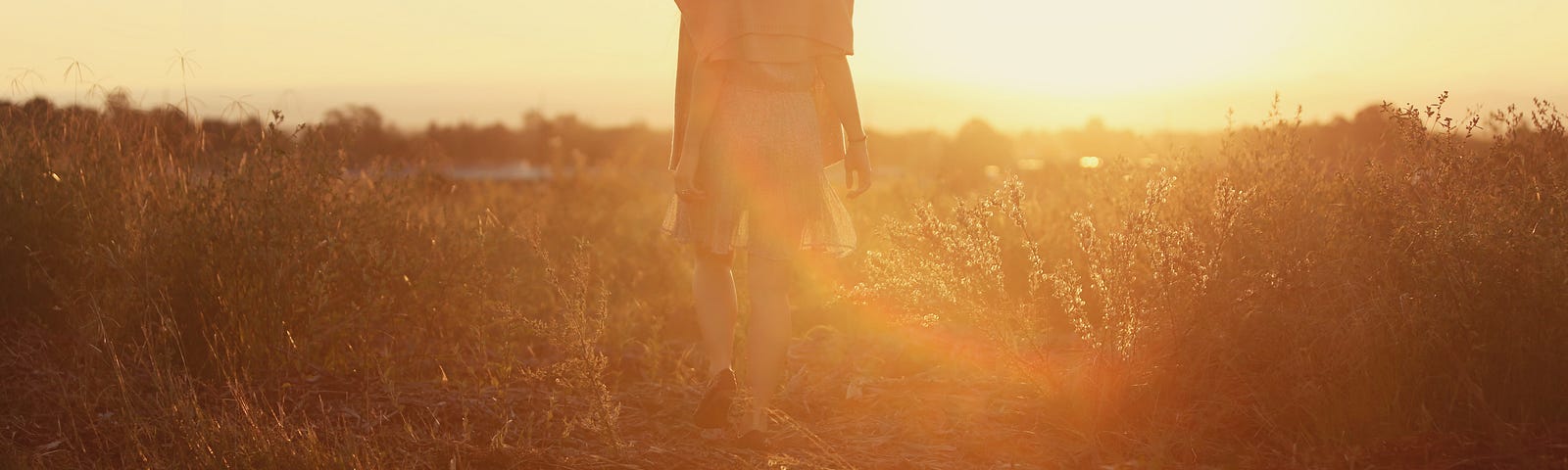 A woman wearing a hat, walking through a sunny field