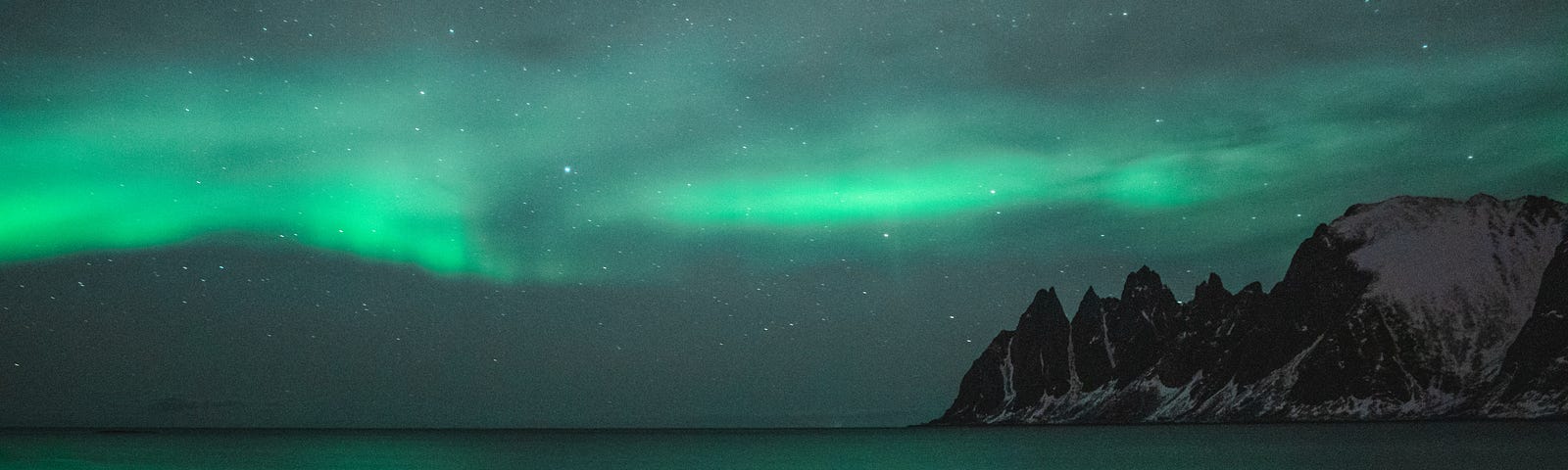 a dark night with the emerald green northern lights on top of the sea