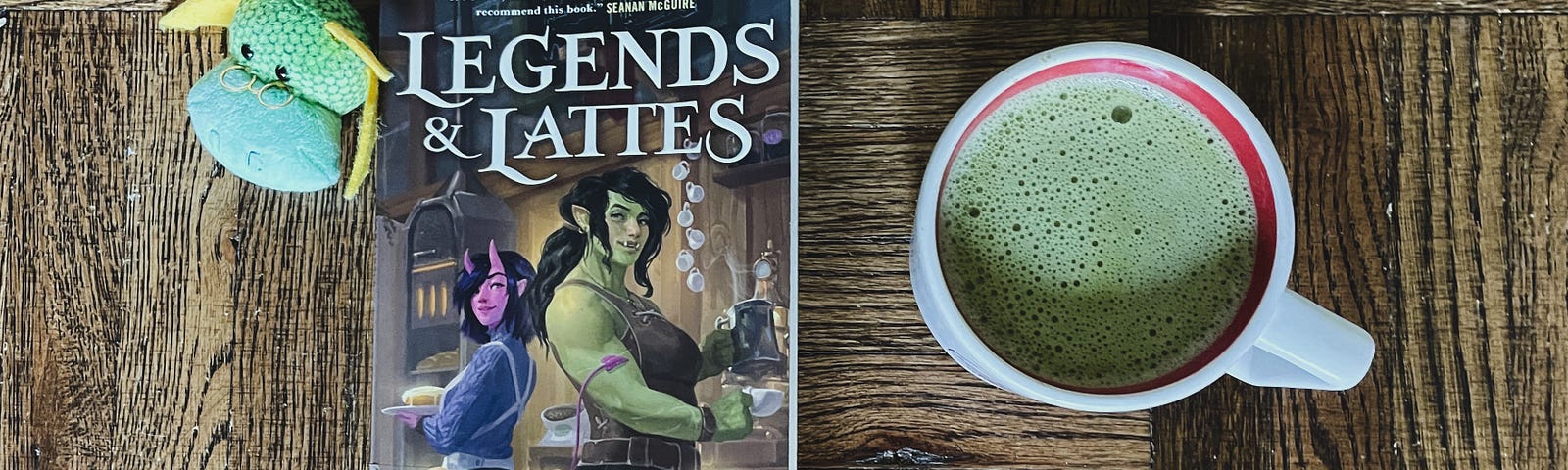 A copy of “Legends & Lattes” by Travis Baldree, with a dragon-shaped bookmark and a matcha latte.