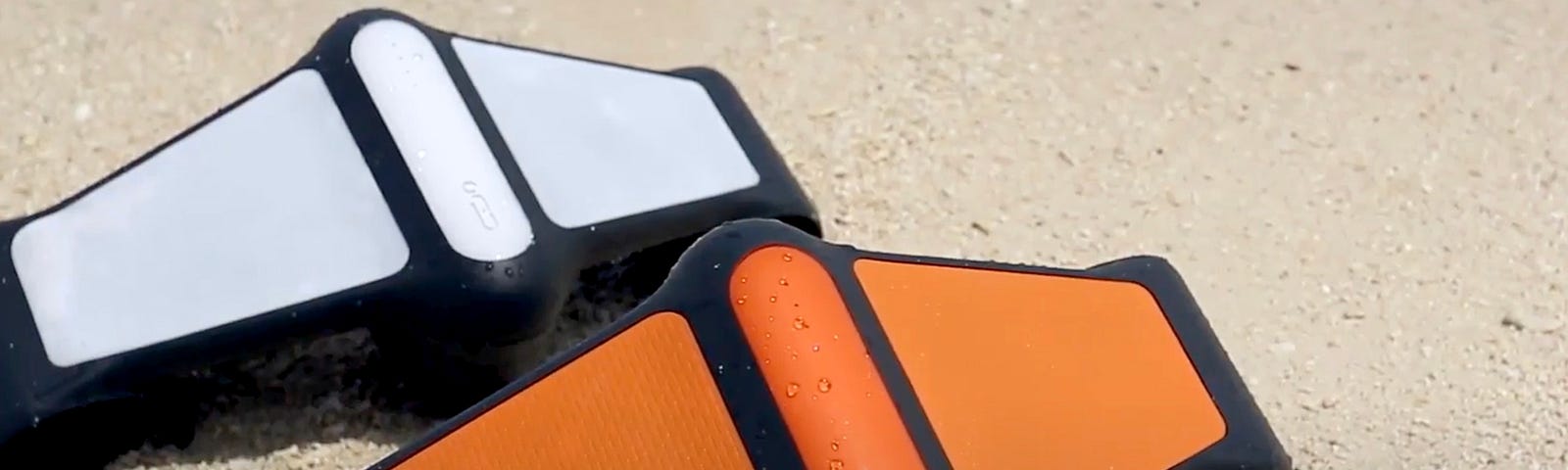 Two Geneinno S1 Pro underwater white and orange scooters sitting side-by-side on a sandy beach.