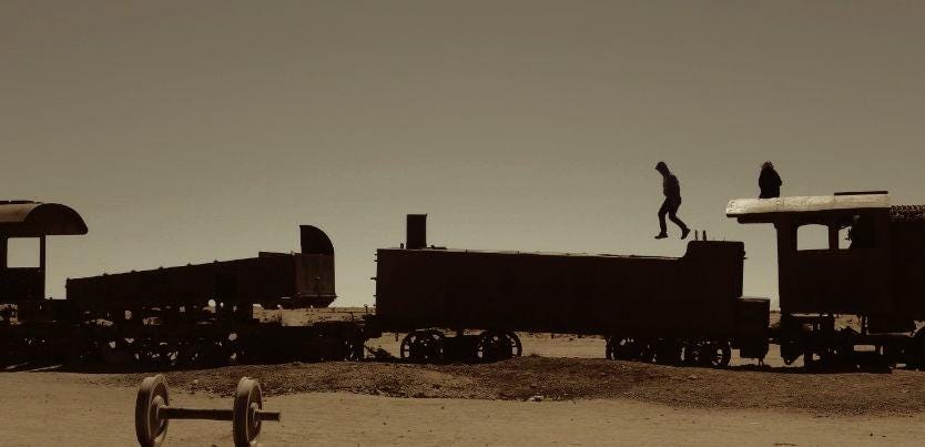 Au milieu d’un desert, au dessus d’un wagon à l’abandon, une personne saute comme si elle s’envolait.