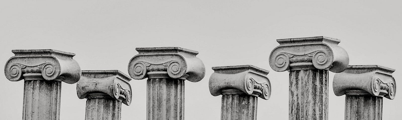 The top halves of 6 ancient pillars in greyscale.