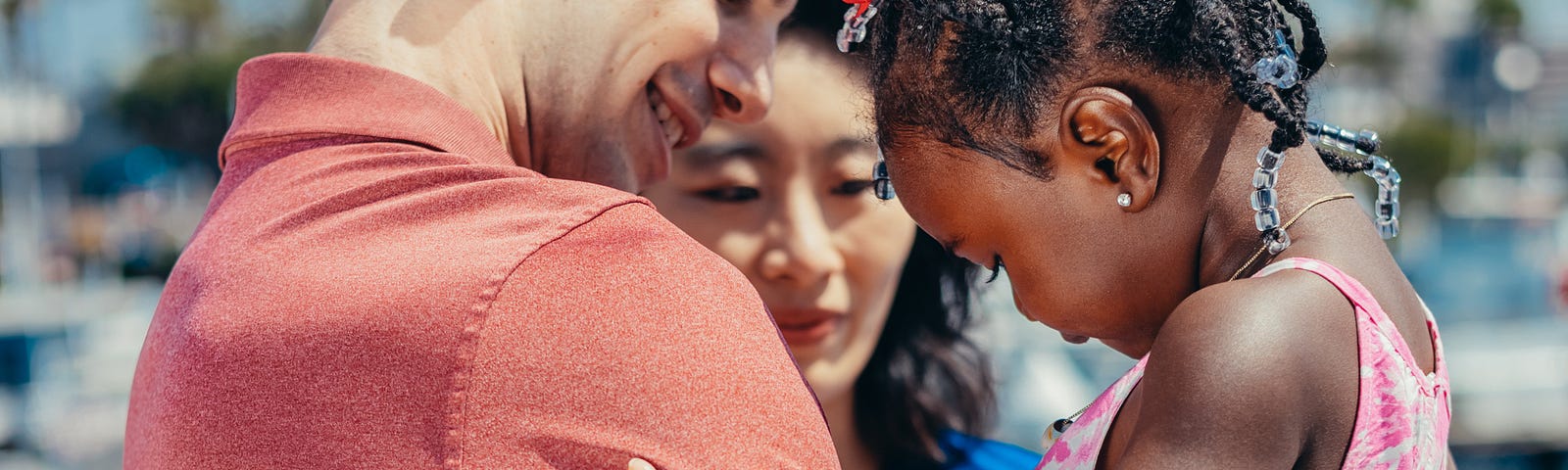 While man, Asian woman hugging black girl