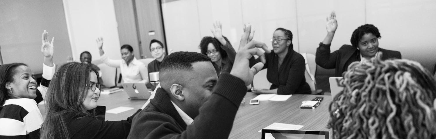 A group of people with hands raised sitting around a desk.