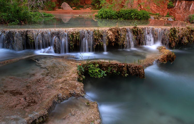 landscape of small waterfalls from the perspective of a blue river in the middle of a forest