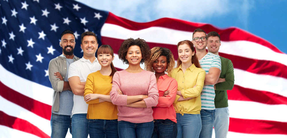 Eight people from diverse backgrounds stand with arms crossed in front of an American flag.