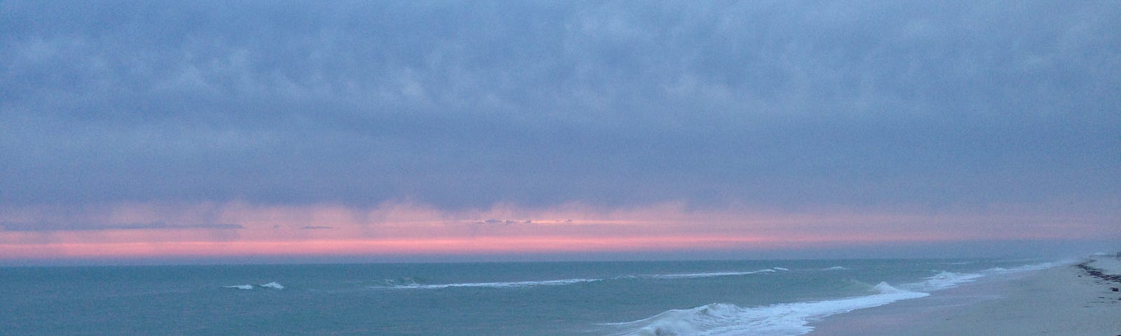 Waves on the sand, with dusky clouds and a pink stripe in the sky