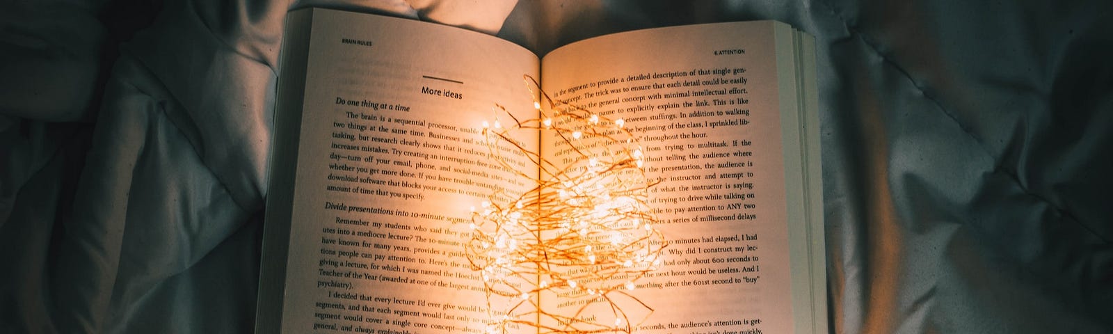 IMAGE: Two hands holding an open book with a chain of lights lit in the middle of the pages